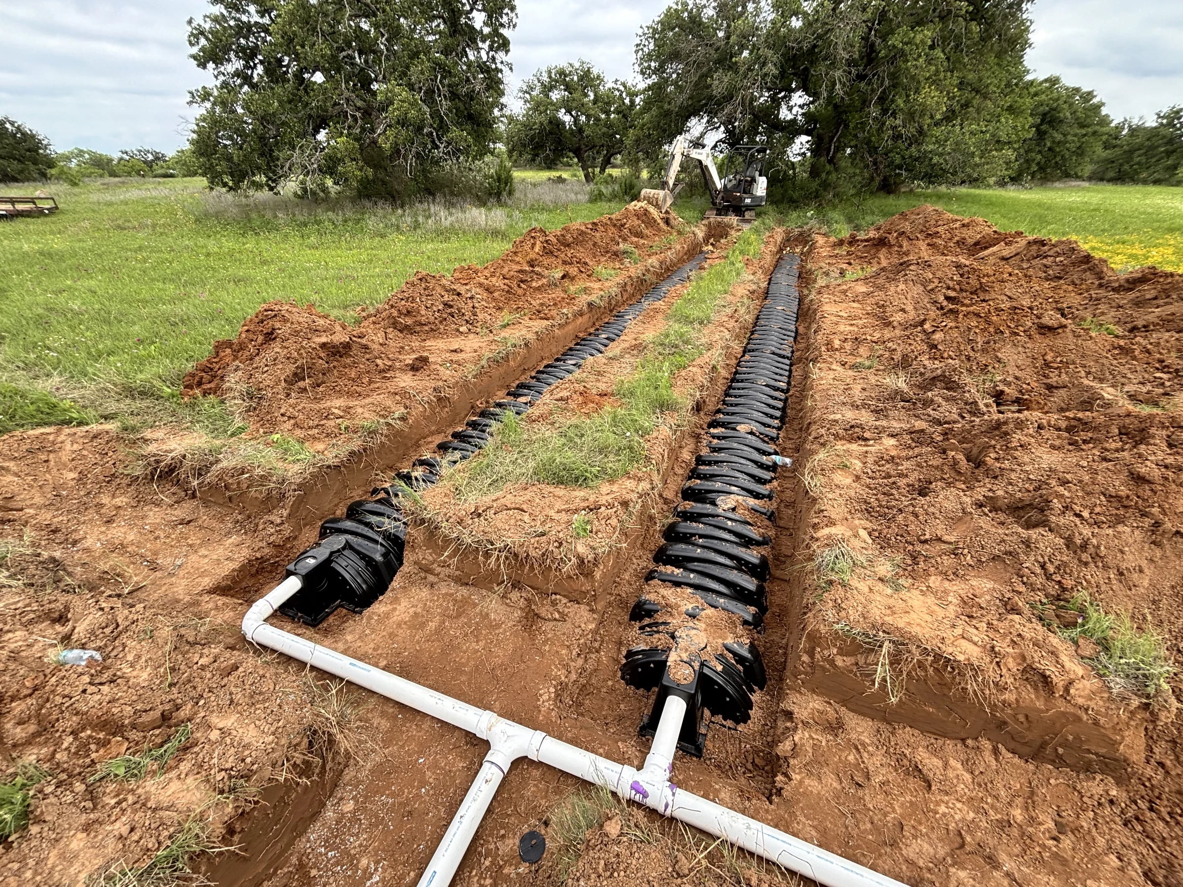Rows of drainfield chambers and white distribution piping across an excavated site