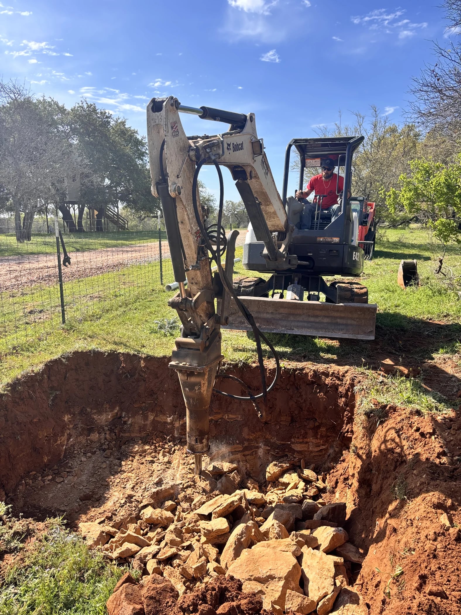 Excavator breaking rock while preparing a septic tank pit