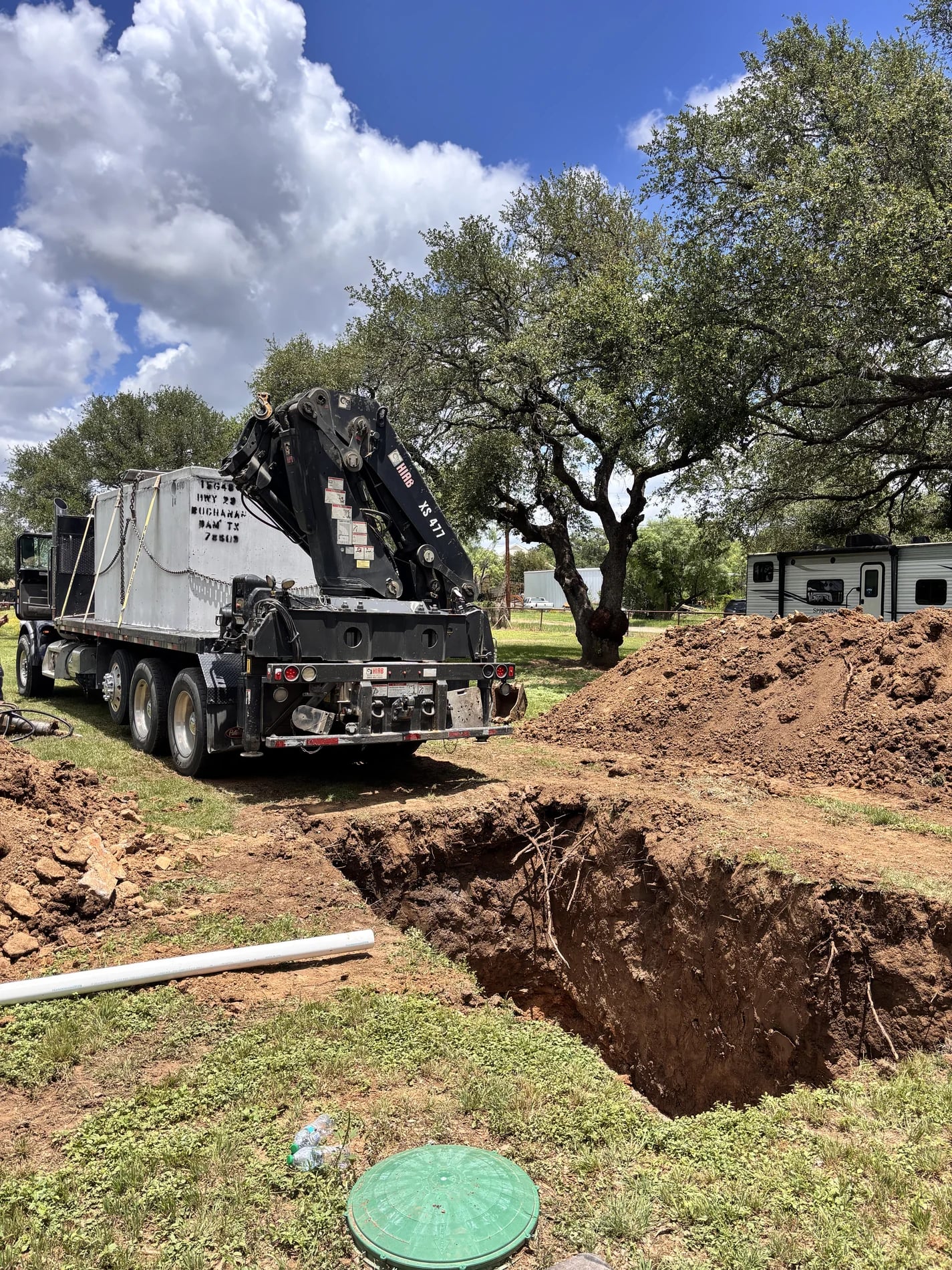 Concrete septic tank on a crane truck beside an excavated tank pit